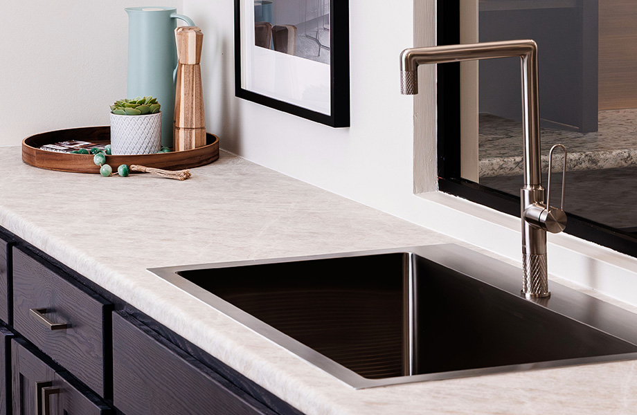 Kitchen with dark wood cabinets and light, stone-look countertop with modern faucet against a window